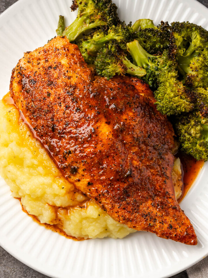 Cast iron skillet chicken on a plate over mashed potatoes.