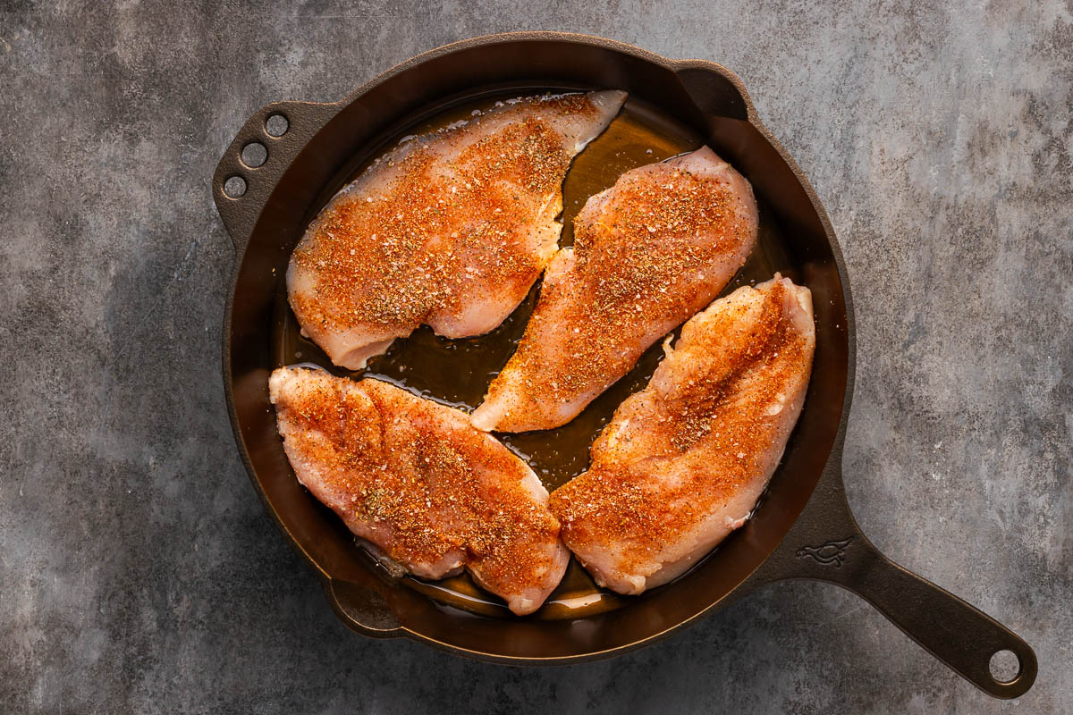 Seasoned chicken put on a cast iron skillet.
