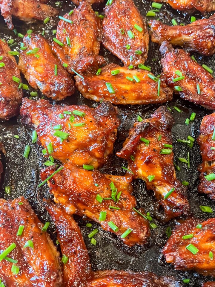 Smoked maple bourbon chicken wings glazed and garnished with chives on a flat cast iron griddle.