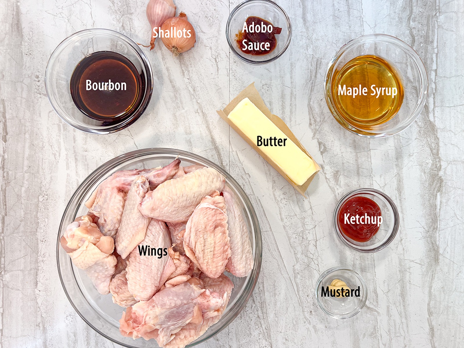 Ingredients to make smoked maple bourbon chicken wings, including ranch dressing mix, maple syrup, bourbon, butter, shallots, ketchup, Dijon mustard, and adobo sauce.