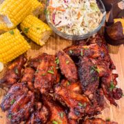 Smoked maple bourbon chicken wings plated on a wooden platter with corn on the cob and coleslaw.