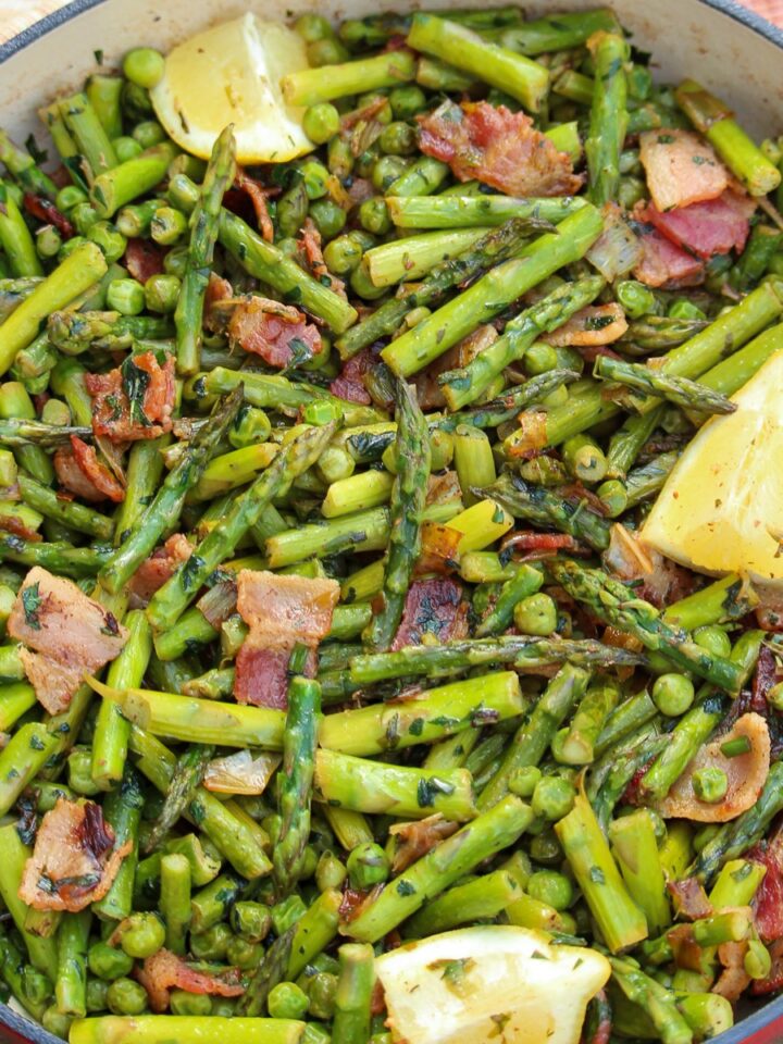 Asparagus and peas recipe with bacon, leeks, and fresh herbs in a red enameled Dutch oven.