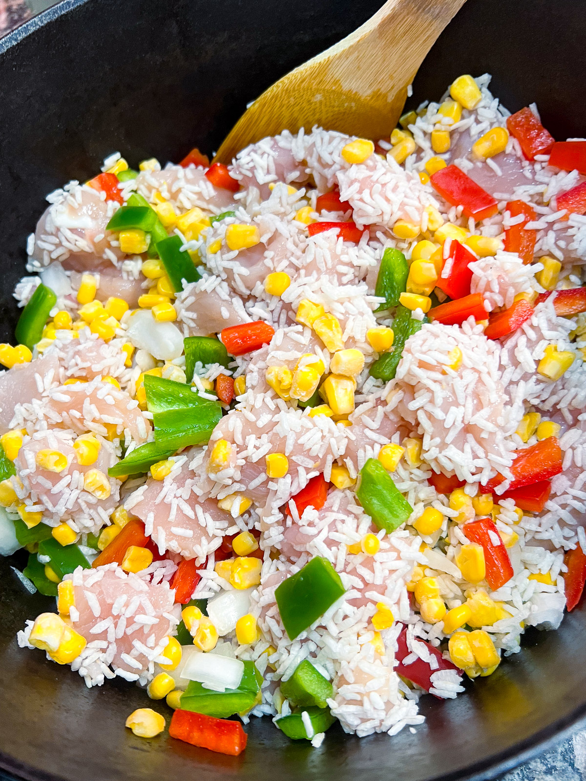 Instant rice, frozen corn, bell peppers, onions, and diced chicken in a dutch oven