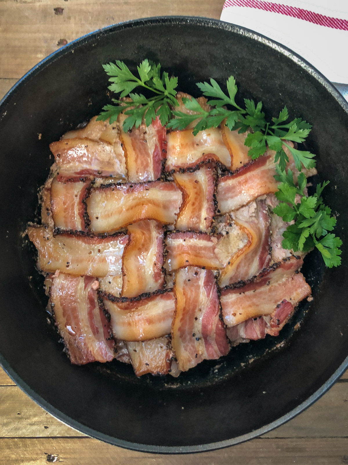Finished bacon wrapped meatloaf in a Dutch oven with crispy bacon lattice and fresh parsley