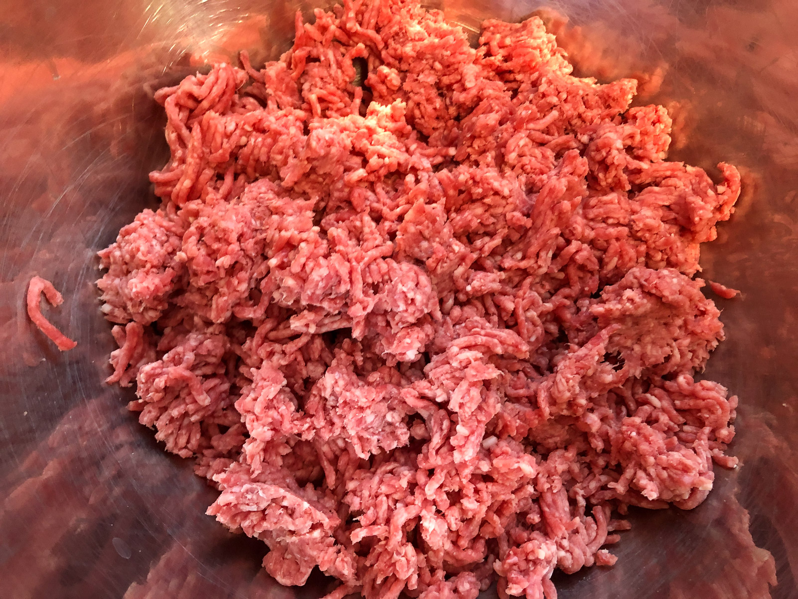 Ground beef crumbled into a stainless steel mixing bowl