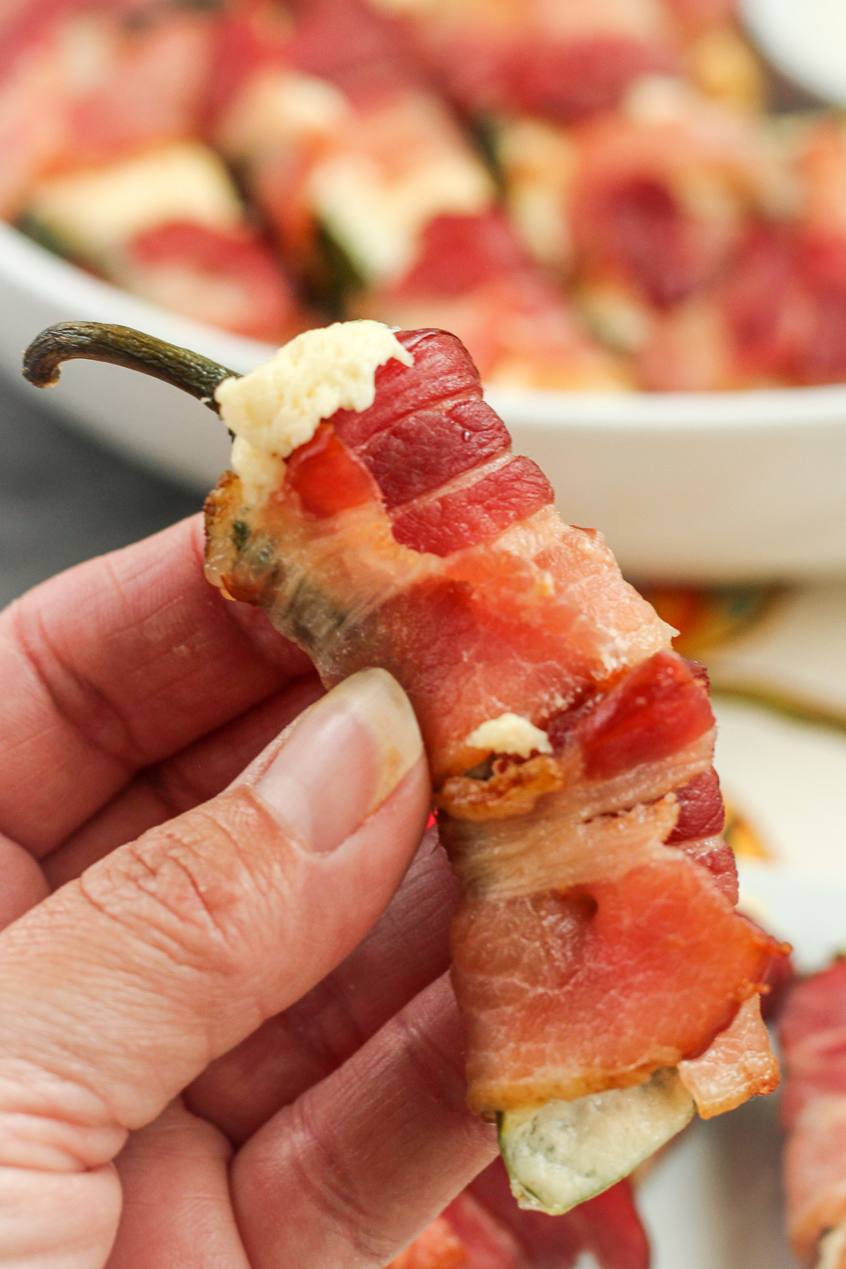 Hand holding a bacon wrapped jalapeno popper showing the creamy filling inside
