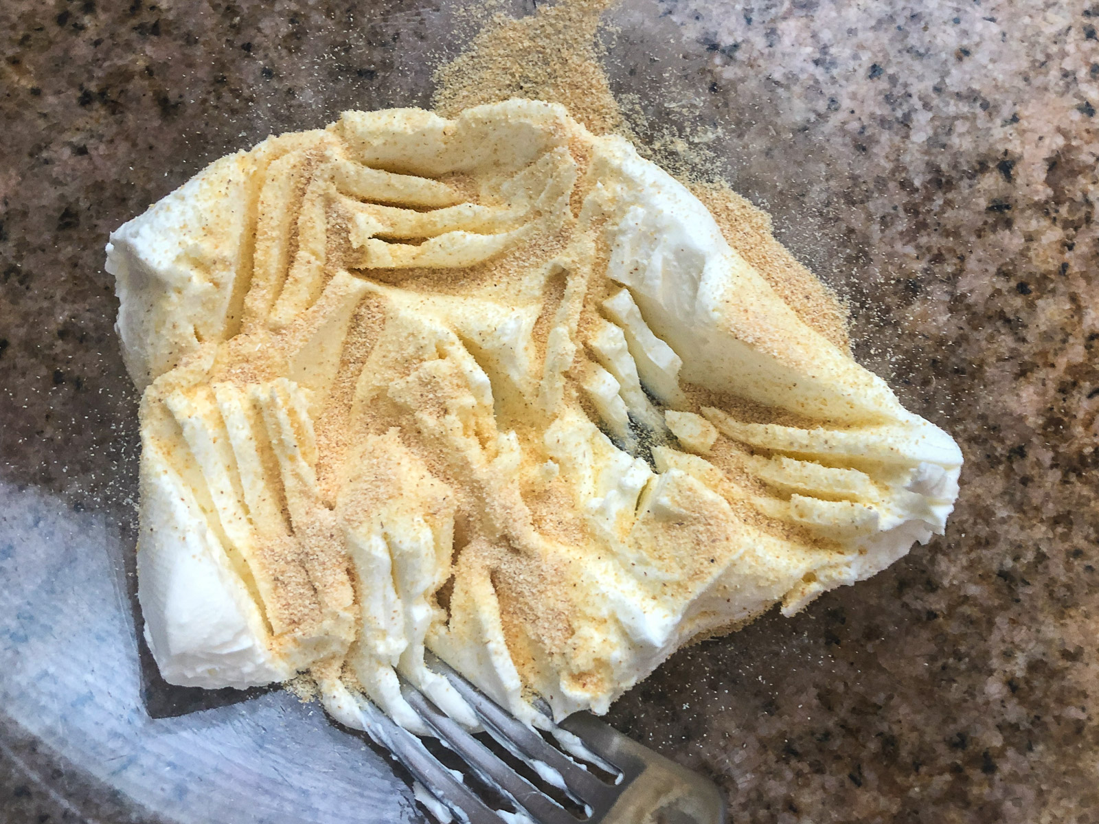 Softened cream cheese being mixed with granulated garlic using a fork