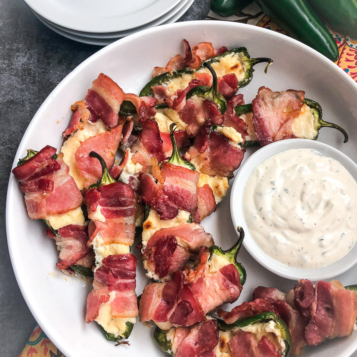 Bacon wrapped jalapeno poppers on a white plate with ranch dip