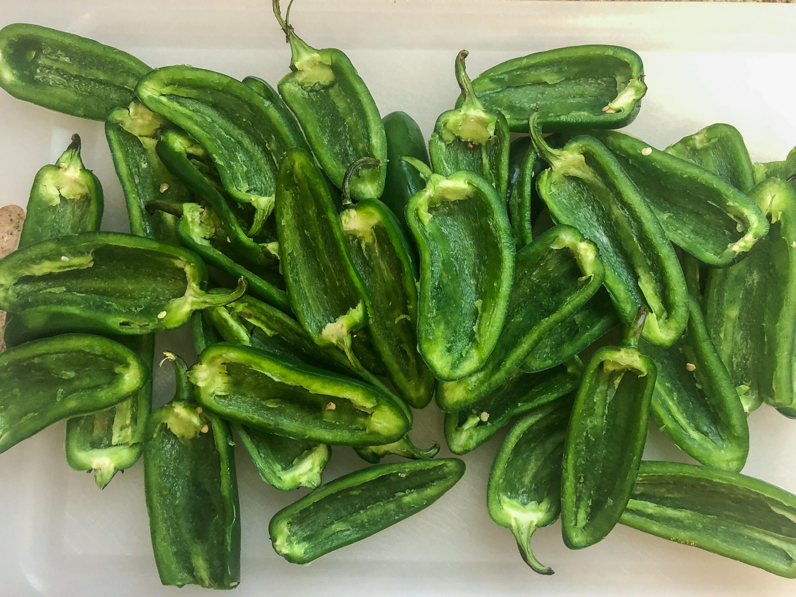 Jalapeno peppers sliced in half with seeds and veins removed on a cutting board