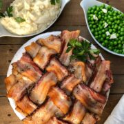 Sliced bacon wrapped meatloaf on a white serving platter with mashed potatoes and peas