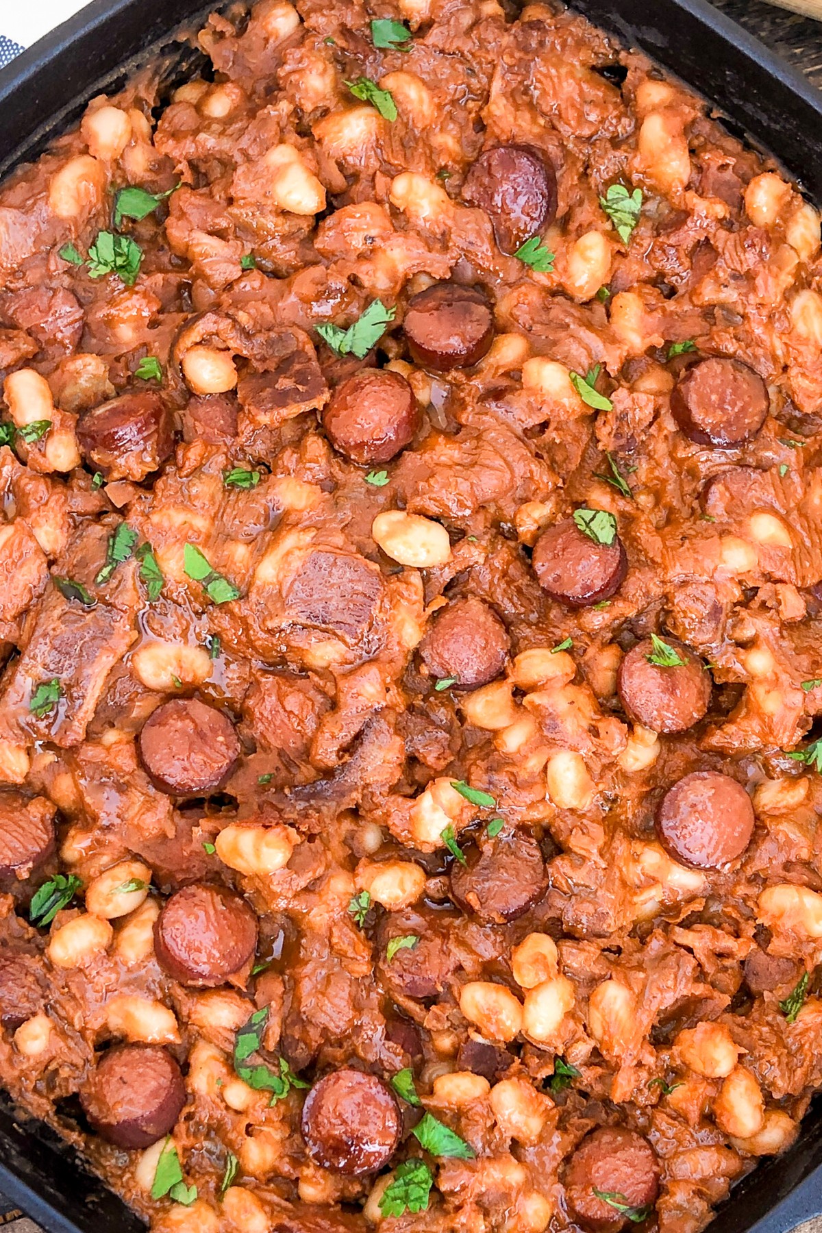 Easy Skillet Beanie Weenies in a cast iron skillet, hot dogs seared and mixed with baked beans.