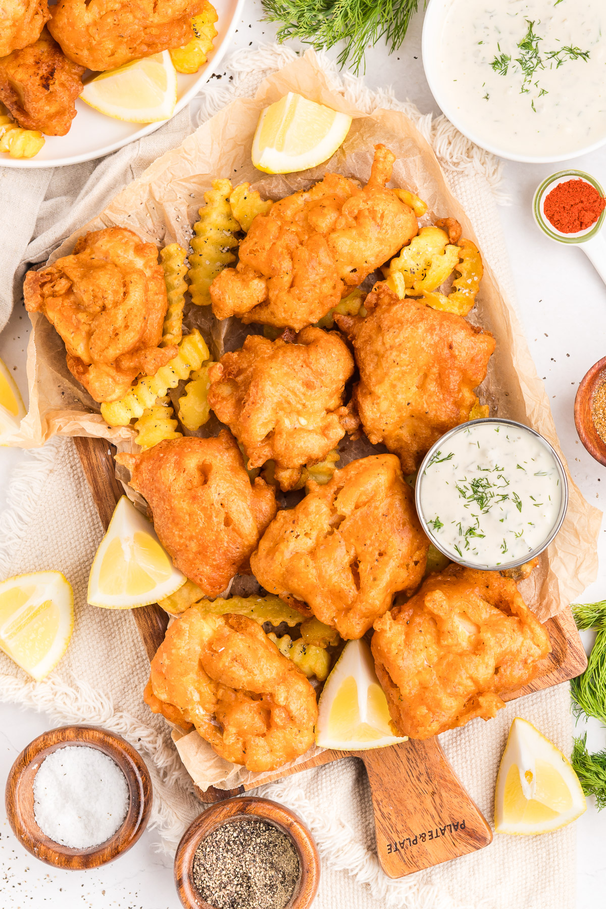 Overhead view of beer battered fish platter with crispy cod, crinkle fries, tartar sauce, lemon wedges, and fresh dill