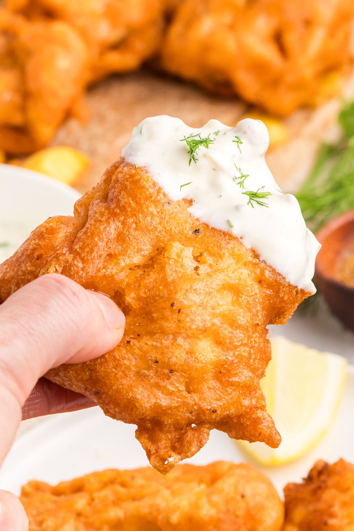 Hand holding a piece of crispy beer battered cod dipped in homemade tartar sauce