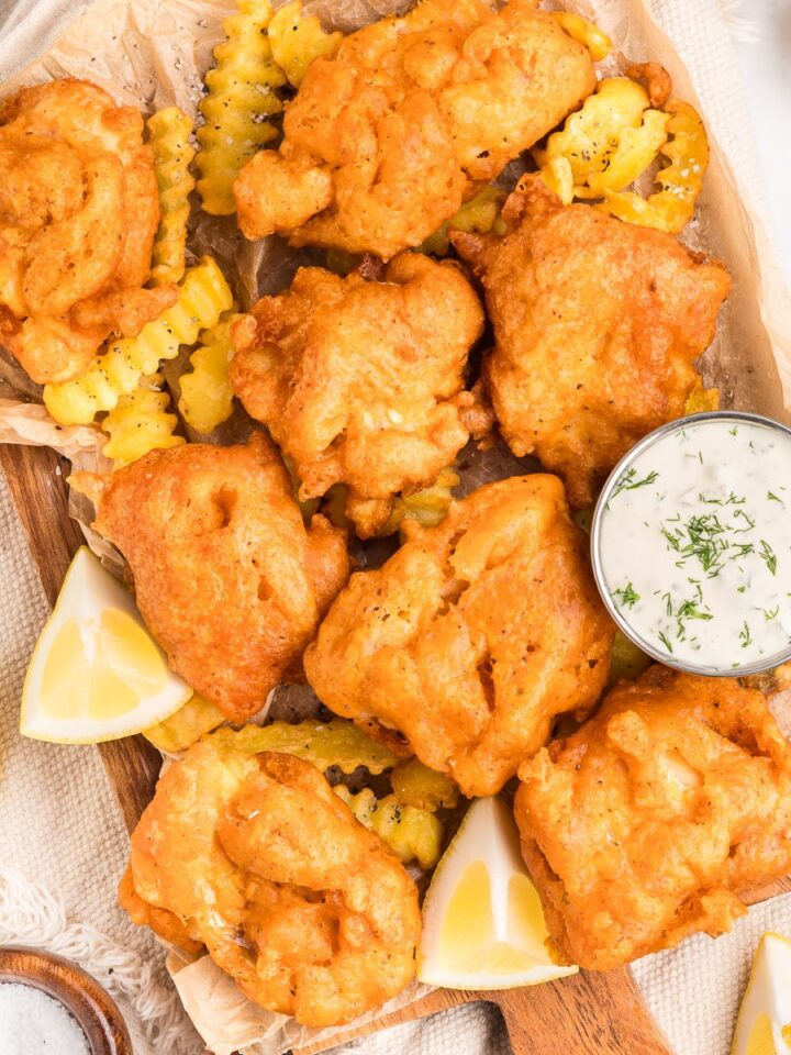 Beer battered fish on a wooden platter with fries, tartar sauce, and lemon wedges