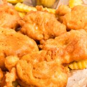 Close-up of crispy beer battered cod pieces on parchment paper with fries