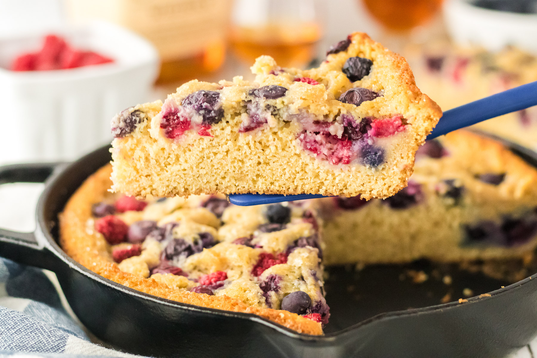 Close up of bourbon berry brown sugar cake in a cast iron skillet showing golden edges and baked berries