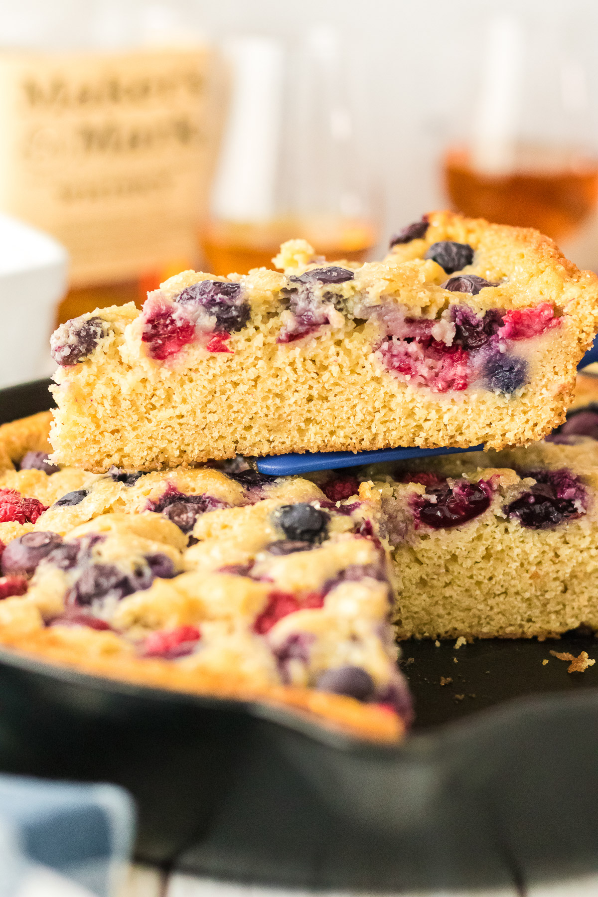 Slice of bourbon berry brown sugar cake being lifted from a cast iron skillet showing moist crumb and berry pockets