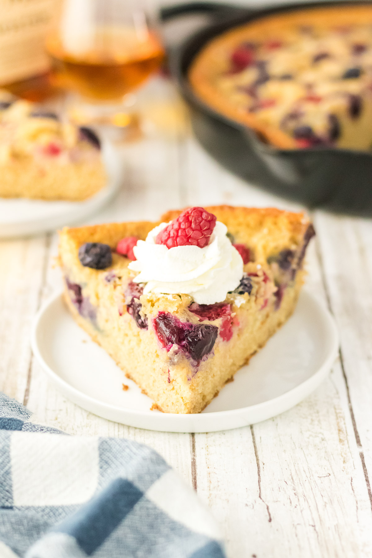 Slice of bourbon berry brown sugar cake on a white plate topped with whipped cream and a fresh raspberry