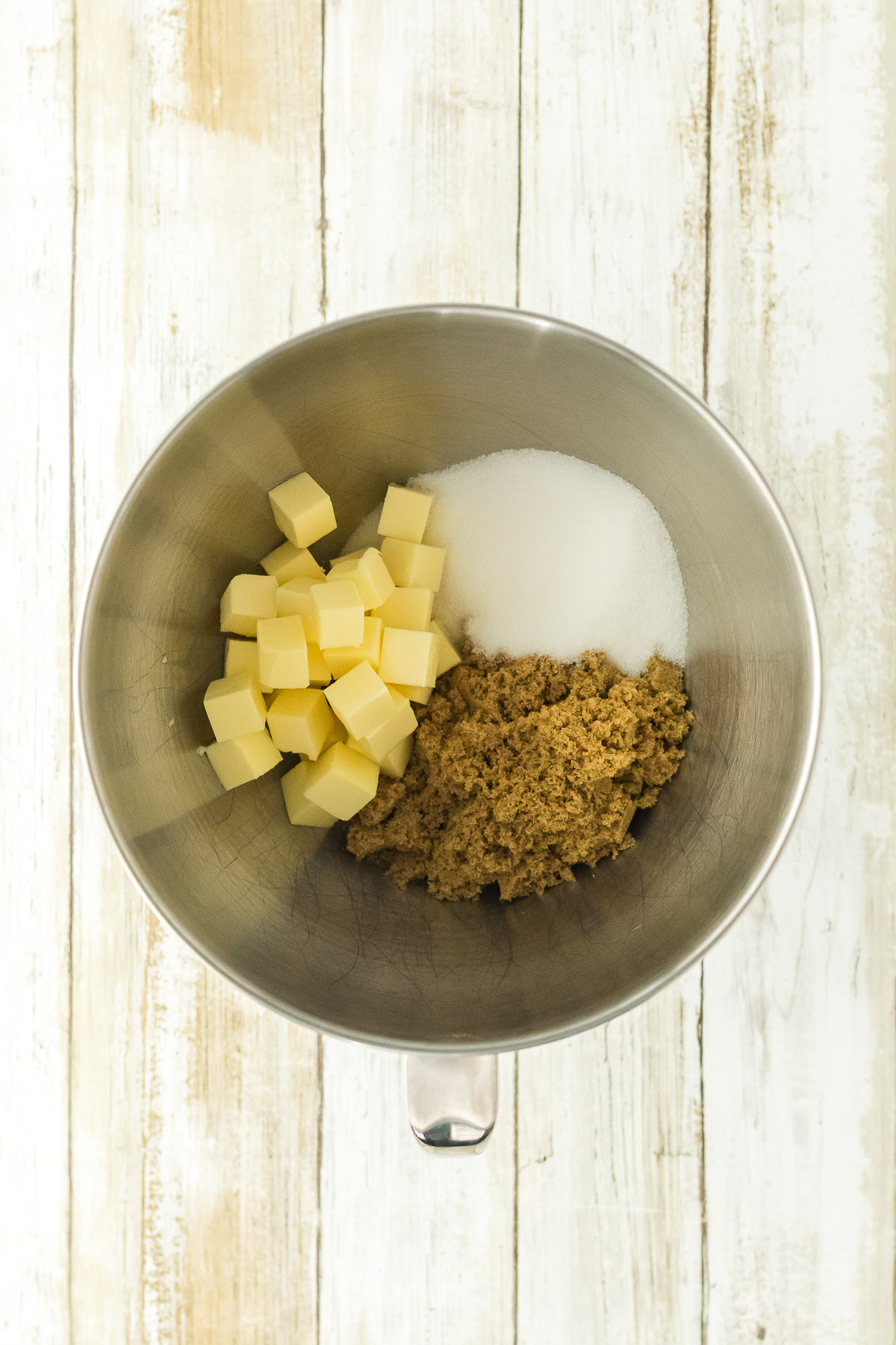 Cubed butter brown sugar and granulated sugar in a stand mixer bowl