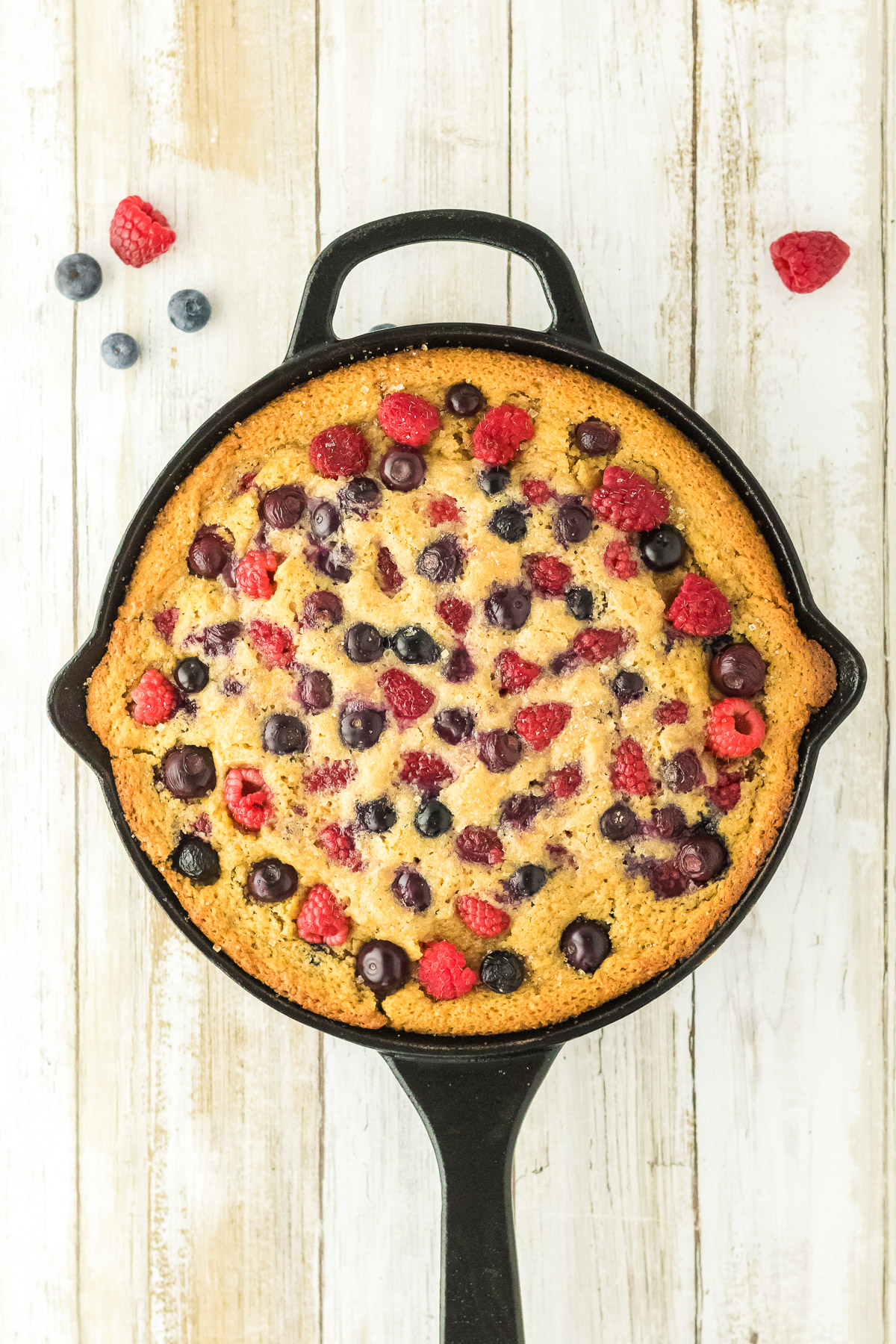 Bourbon berry brown sugar cake in a cast iron skillet topped with baked raspberries and blueberries