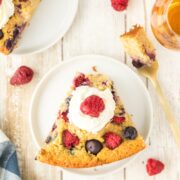 Slice of bourbon berry brown sugar cake on a plate topped with whipped cream and a fresh raspberry