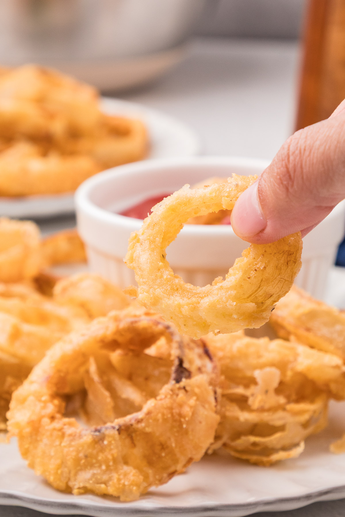 Hand holding a single crispy buttermilk onion ring showing the golden coating