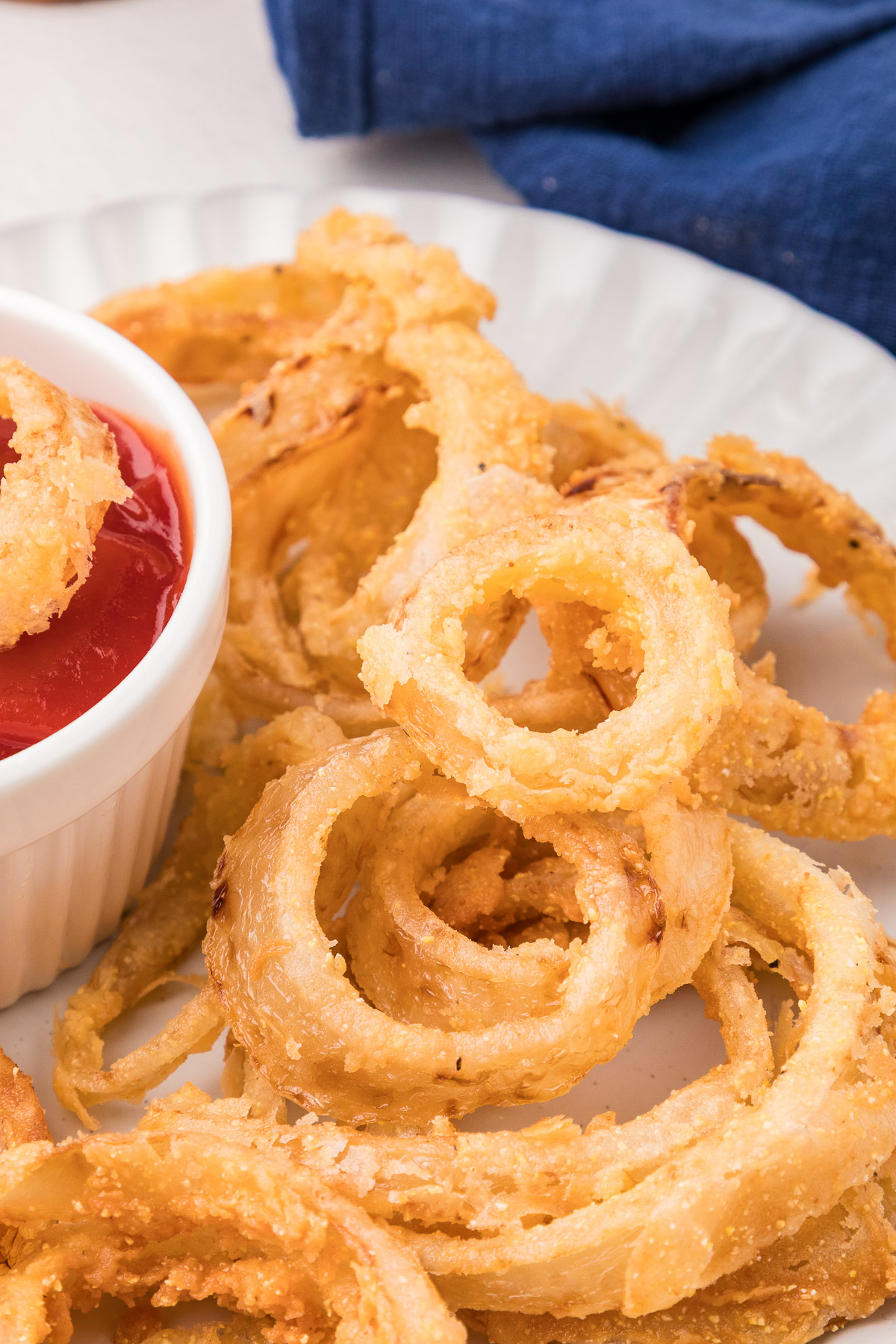 Tall stack of crispy fried rings on a white plate with a side of ketchup