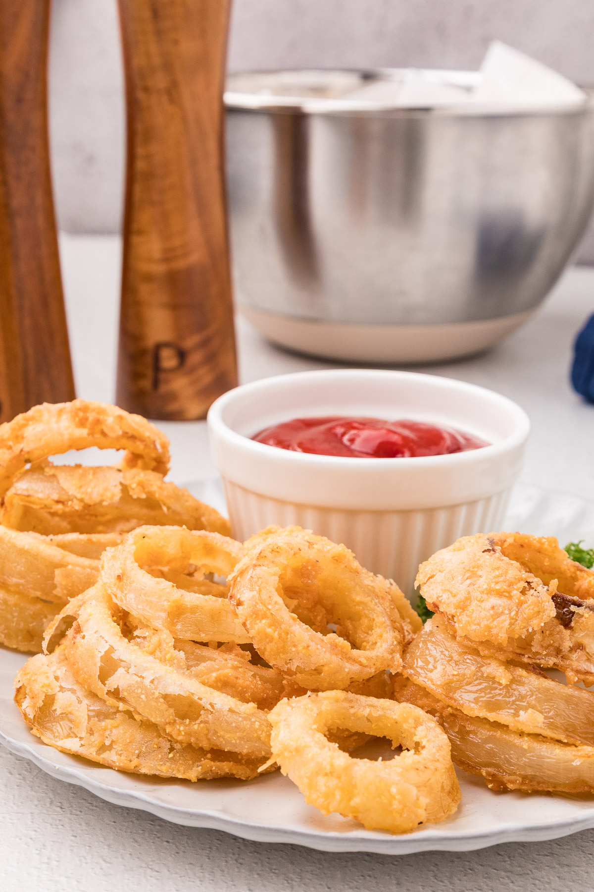 Crispy buttermilk onion rings served on a plate with a ramekin of ketchup and salt and pepper grinders