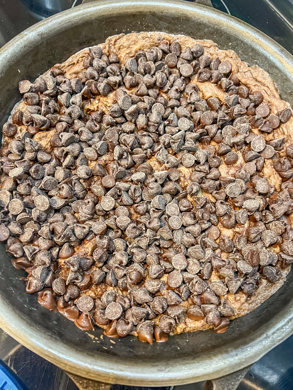 Chocolate chips sprinkled over partially baked brownies in a cast iron skillet.