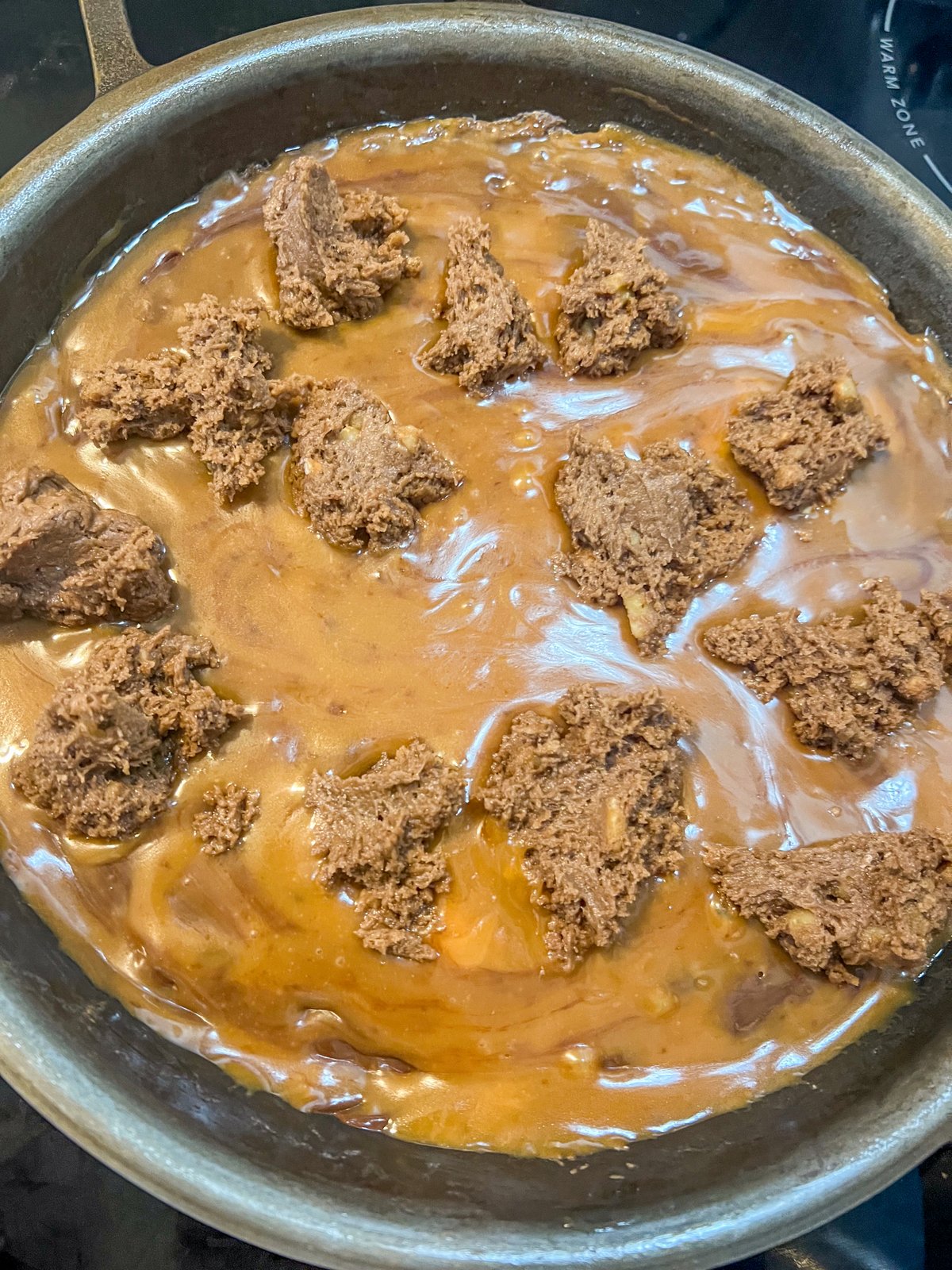 Remaining brownie batter dolloped over the caramel layer in a cast iron skillet.