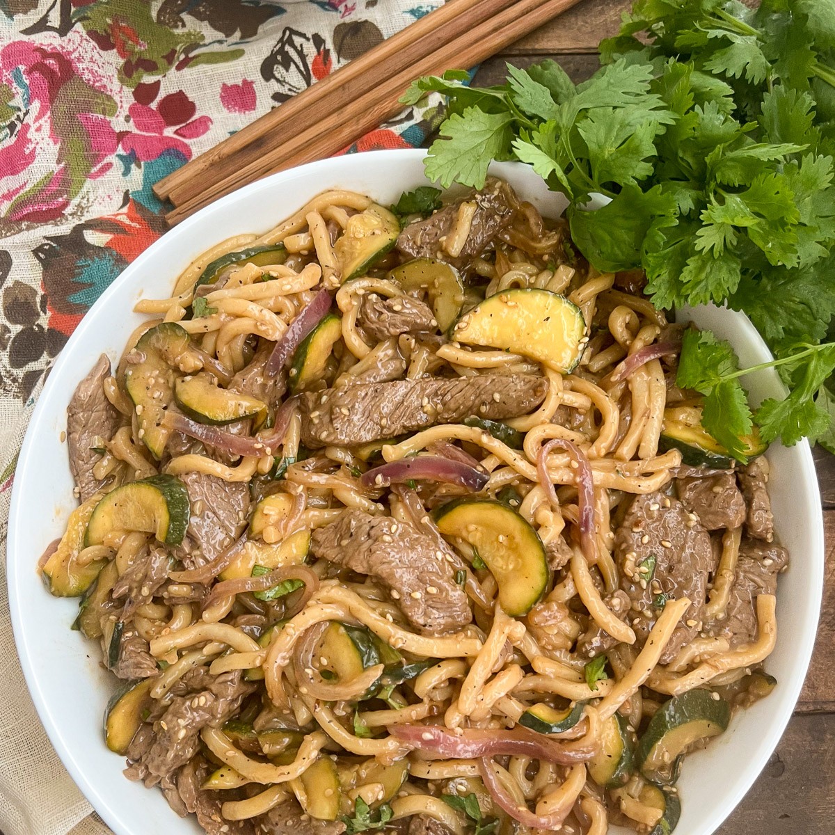 Teriyaki beef udon noodles served in a white bowl with cilantro and sesame seeds.