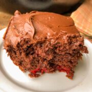 A slice of frosted cherry chocolate cake on a white plate.