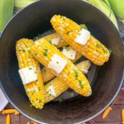 Freshly steamed corn on the cob in a dutch oven with butter and chopped parsley.