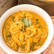 Bowl of butternut tortellini sausage soup in a white bowl garnished with fresh sage leaves.