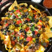 Cast iron skillet nachos loaded with toppings and served with a side of salsa