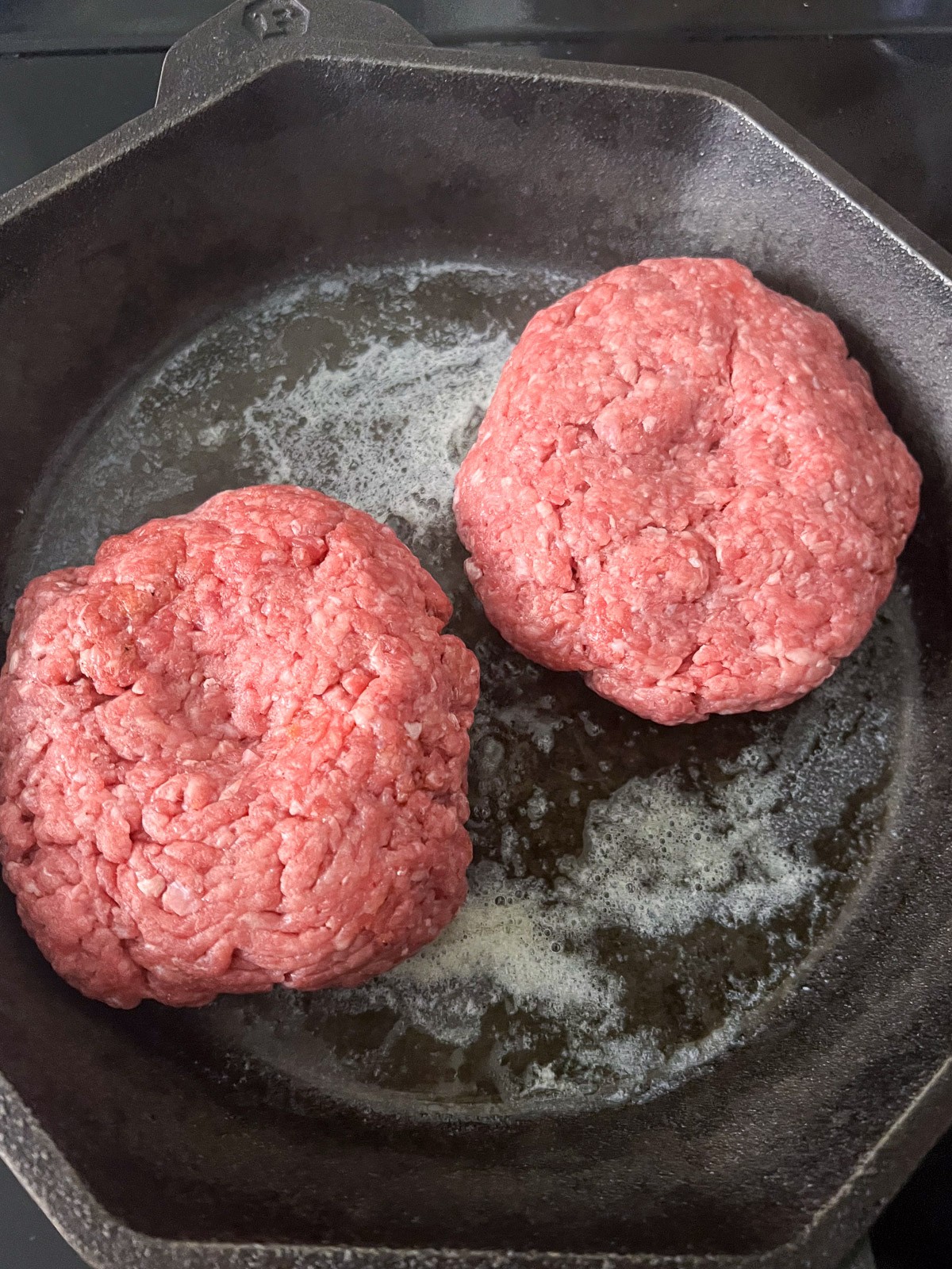Two burgers in a cast iron skillet to cook.