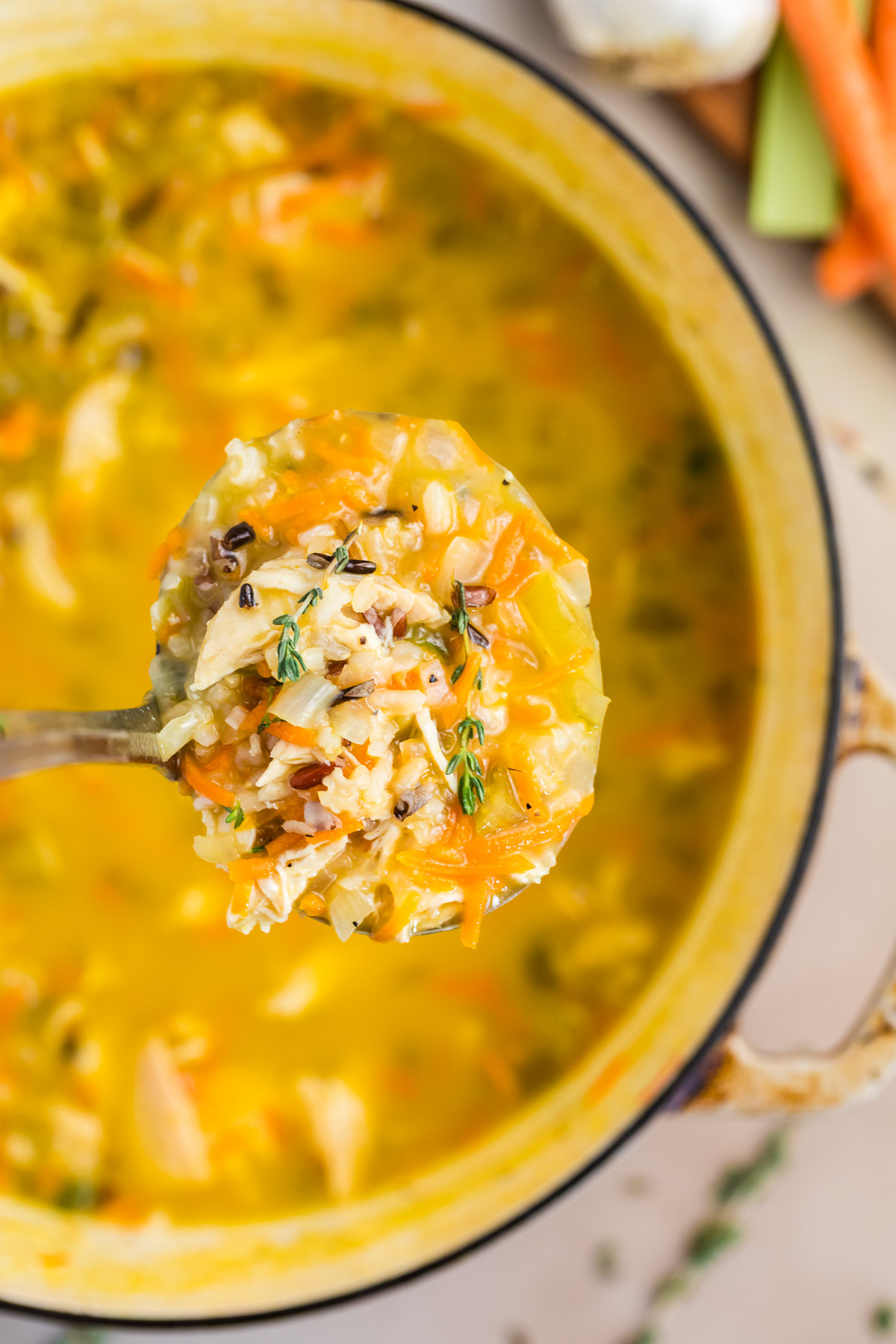 Ladle full of chicken wild rice soup showing shredded chicken, wild rice, carrots, and fresh thyme
