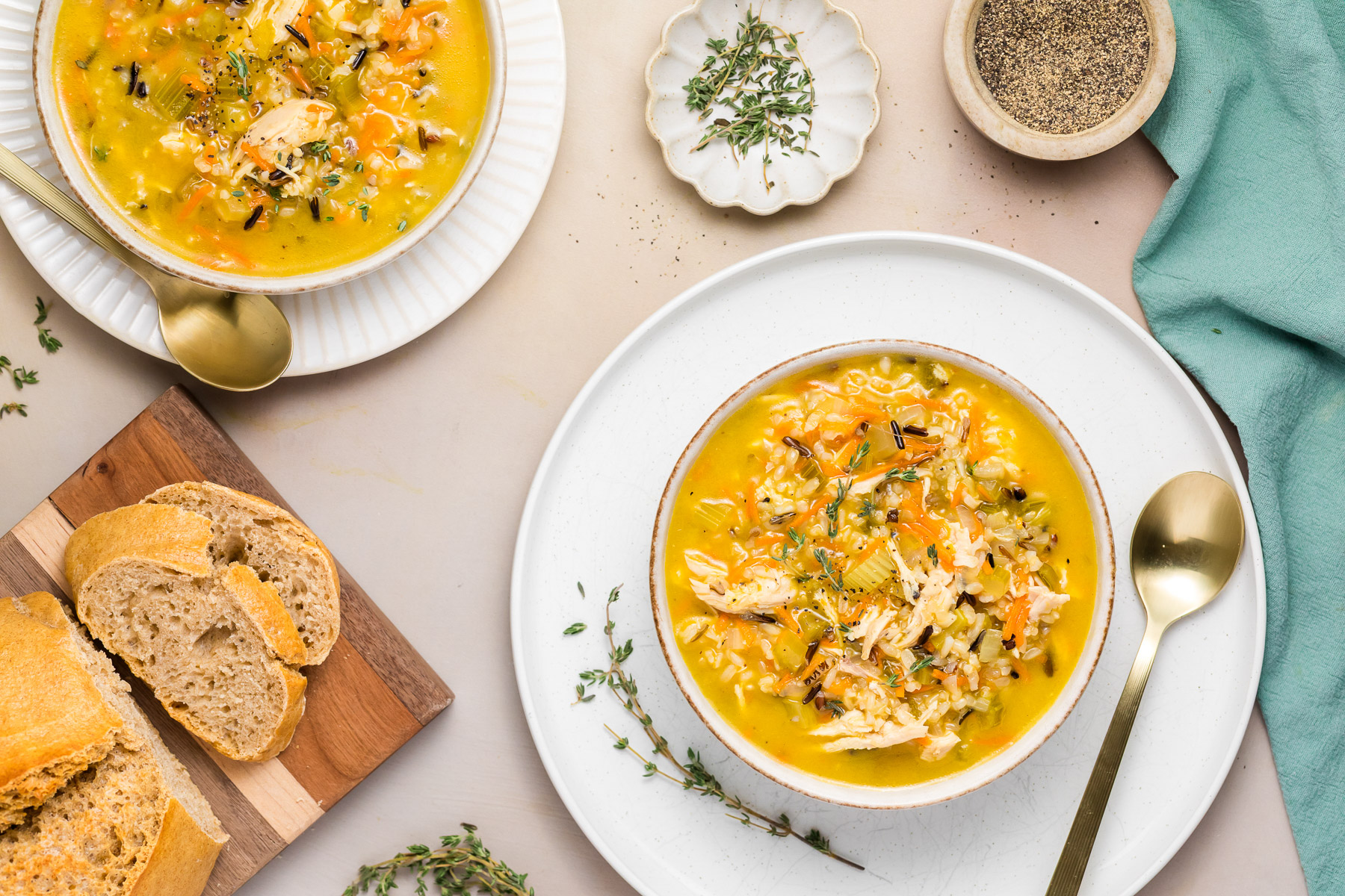 Two bowls of chicken wild rice soup with sliced crusty bread on a cutting board