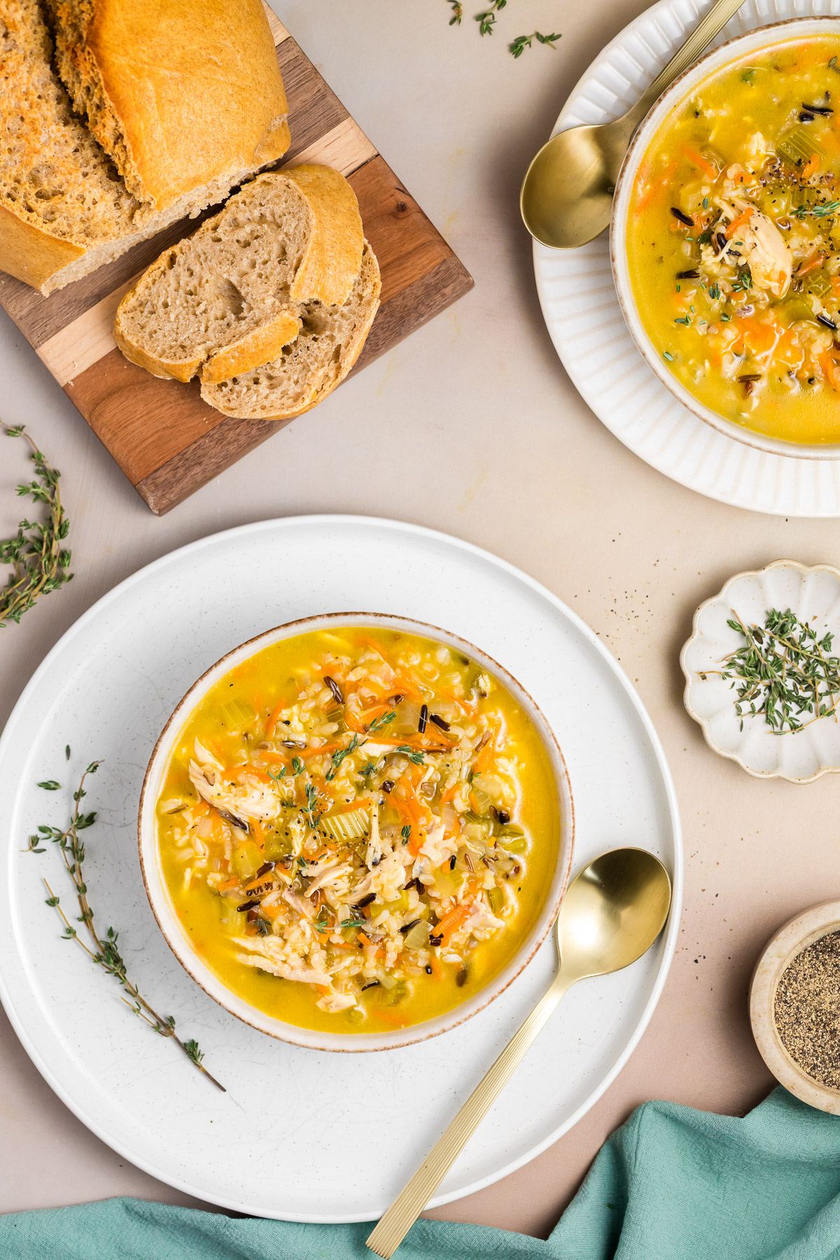 Two bowls of chicken wild rice soup served with crusty bread and fresh thyme in a dutch oven