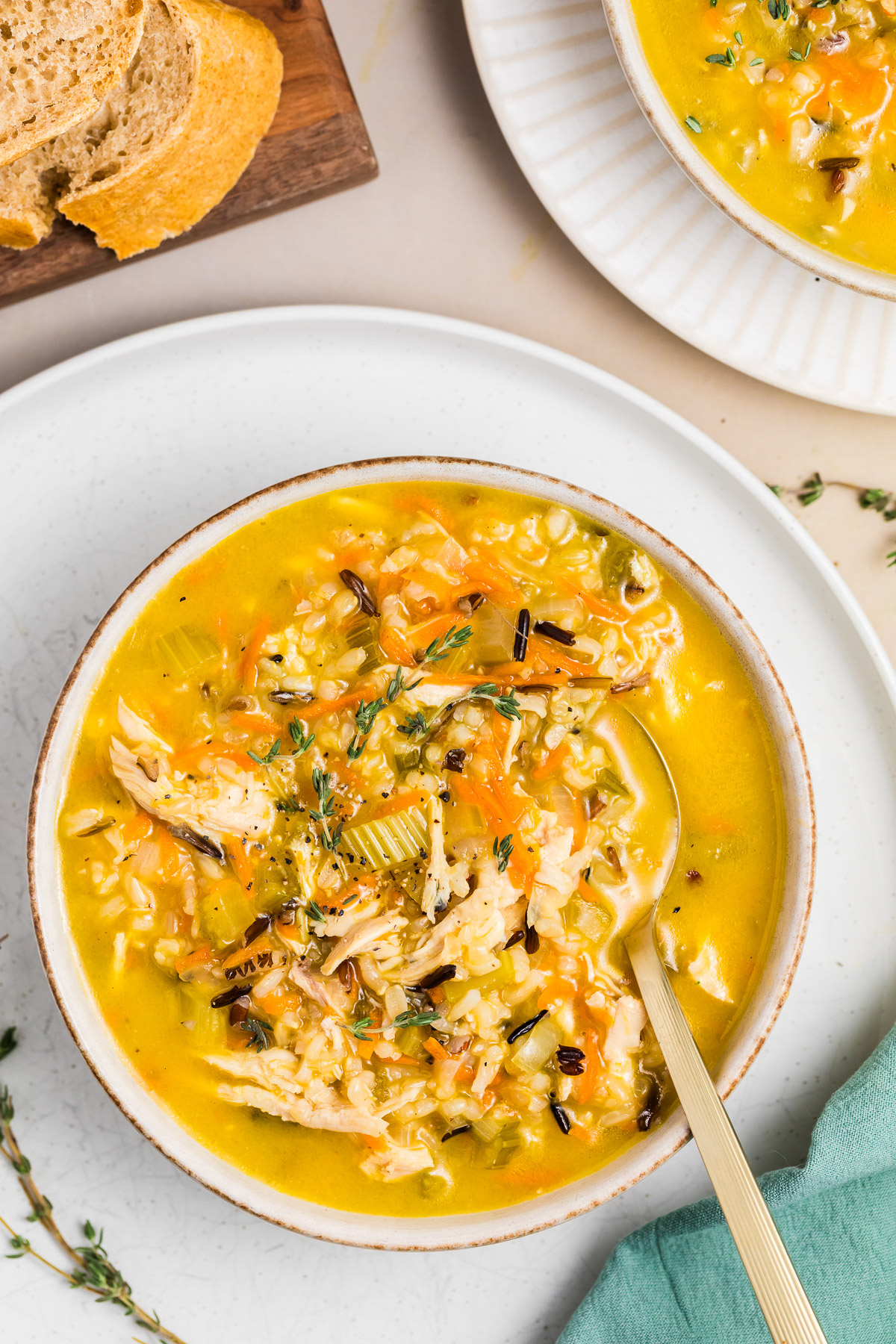 Bowl of chicken wild rice soup with a spoon, topped with fresh thyme and black pepper