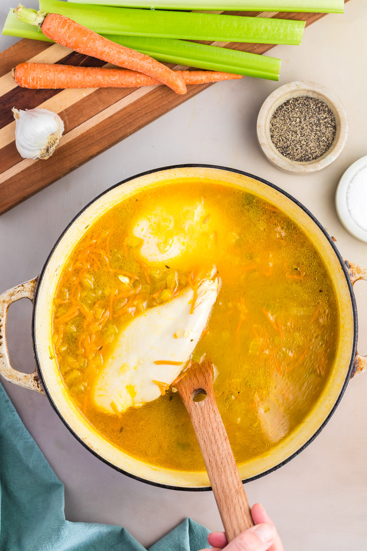 Whole chicken breast added to simmering broth with wild rice and vegetables in a dutch oven