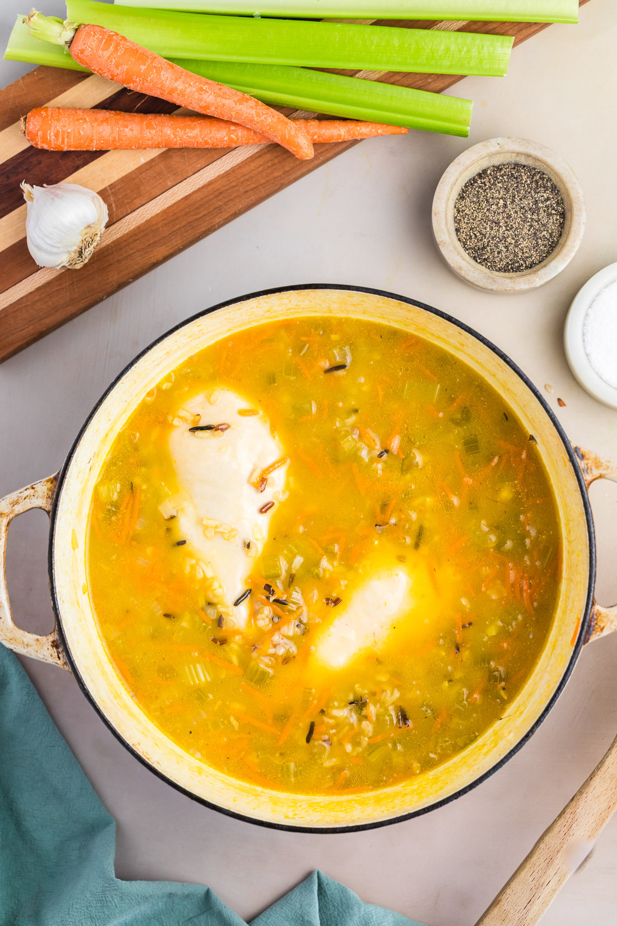 Chicken breasts poaching in broth with wild rice and vegetables in a dutch oven