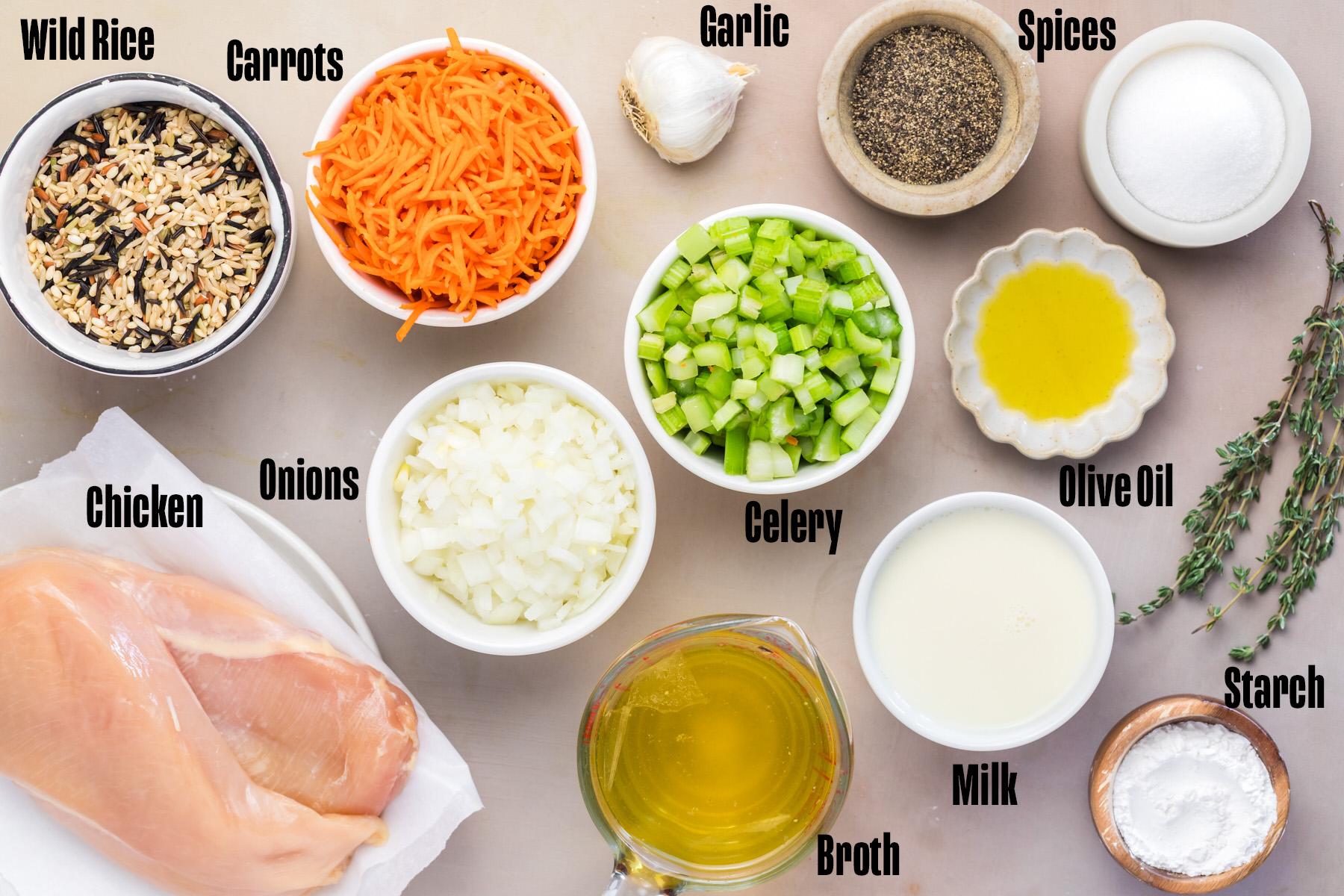 Ingredients for chicken wild rice soup laid out including wild rice, shredded carrots, chicken breast, onions, celery, broth, garlic, olive oil, milk, and arrowroot starch