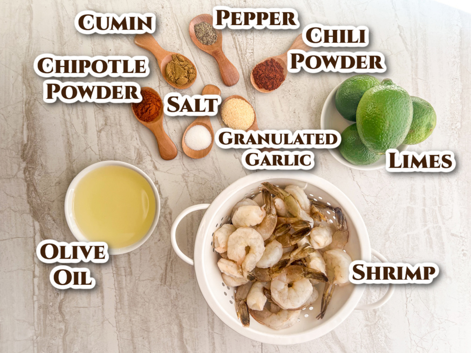 Labeled image of ingredients for the recipe: cumin, pepper, chili powder, salt, granulated garlic, chipotle powder, fresh limes, raw shrimp, and olive oil.