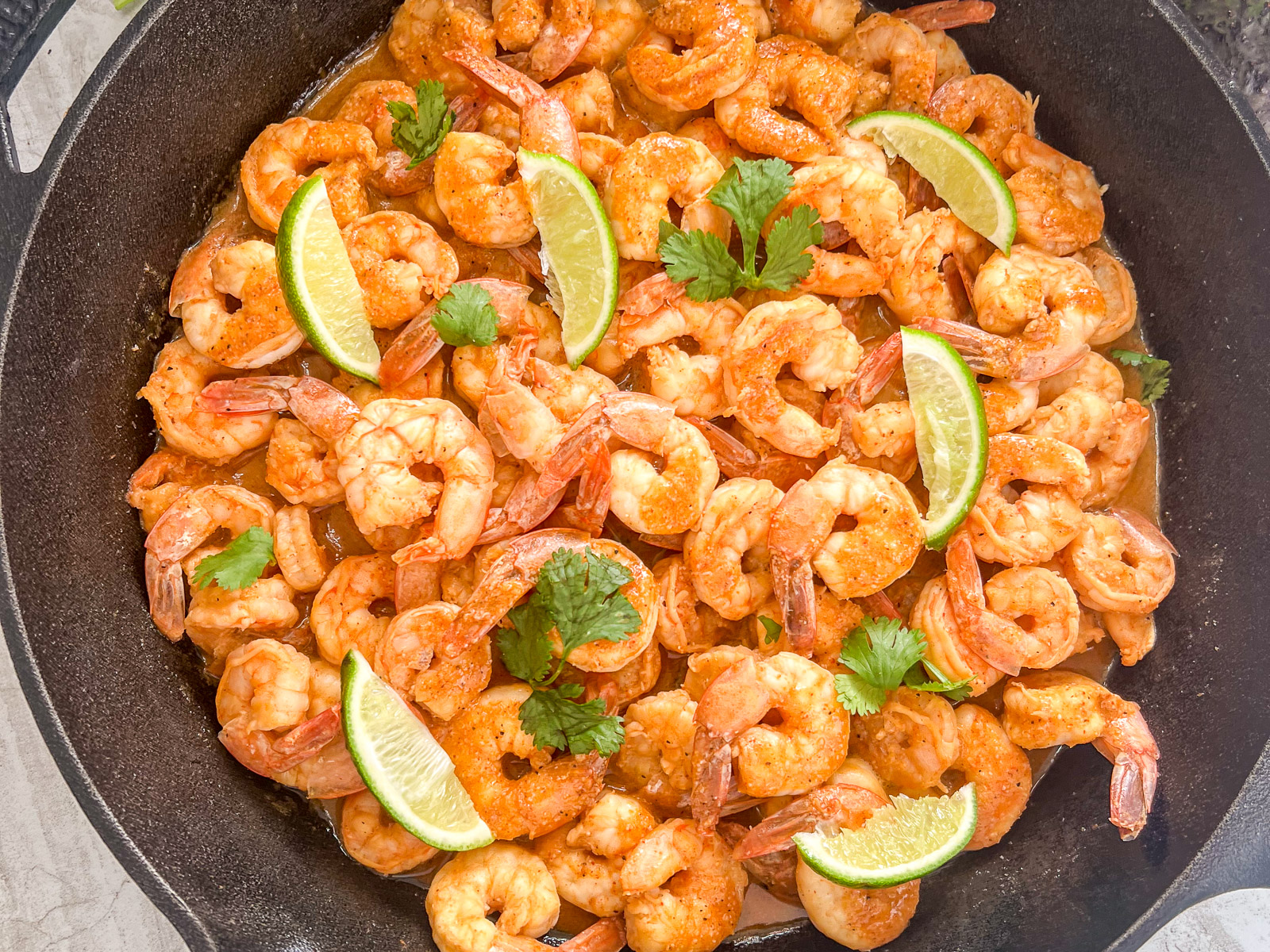 Finished chili lime shrimp in a cast iron skillet garnished with lime wedges and cilantro