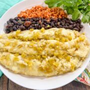 Plated creamy green chile chicken enchiladas topped with sour cream and fresh cilantro.