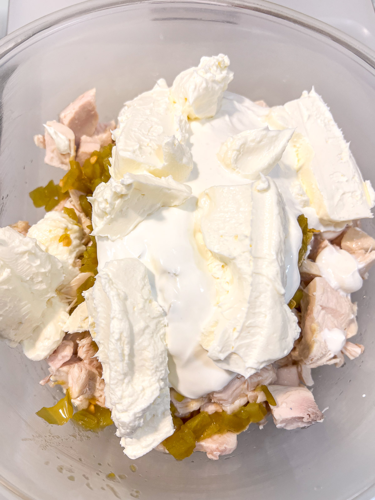 Mixing cream cheese, sour cream, diced green chiles, and shredded chicken in a large bowl