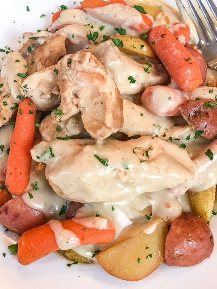 Italian dressing chicken with potatoes and carrots covered in creamy gravy on a white plate.