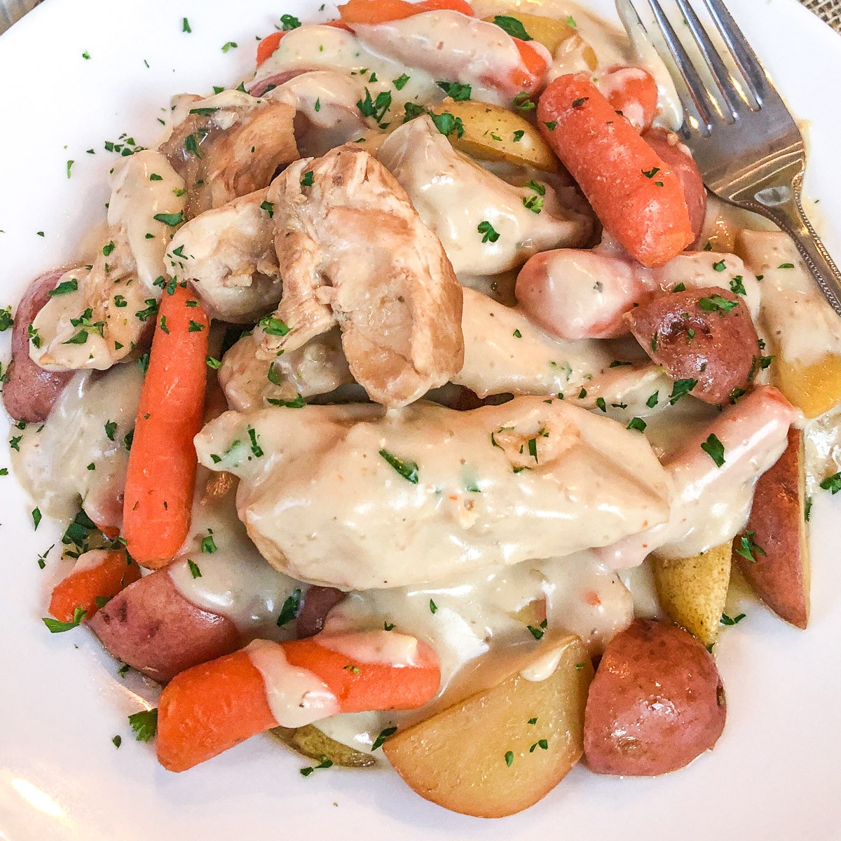 Italian dressing chicken with potatoes and carrots covered in creamy gravy on a white plate.
