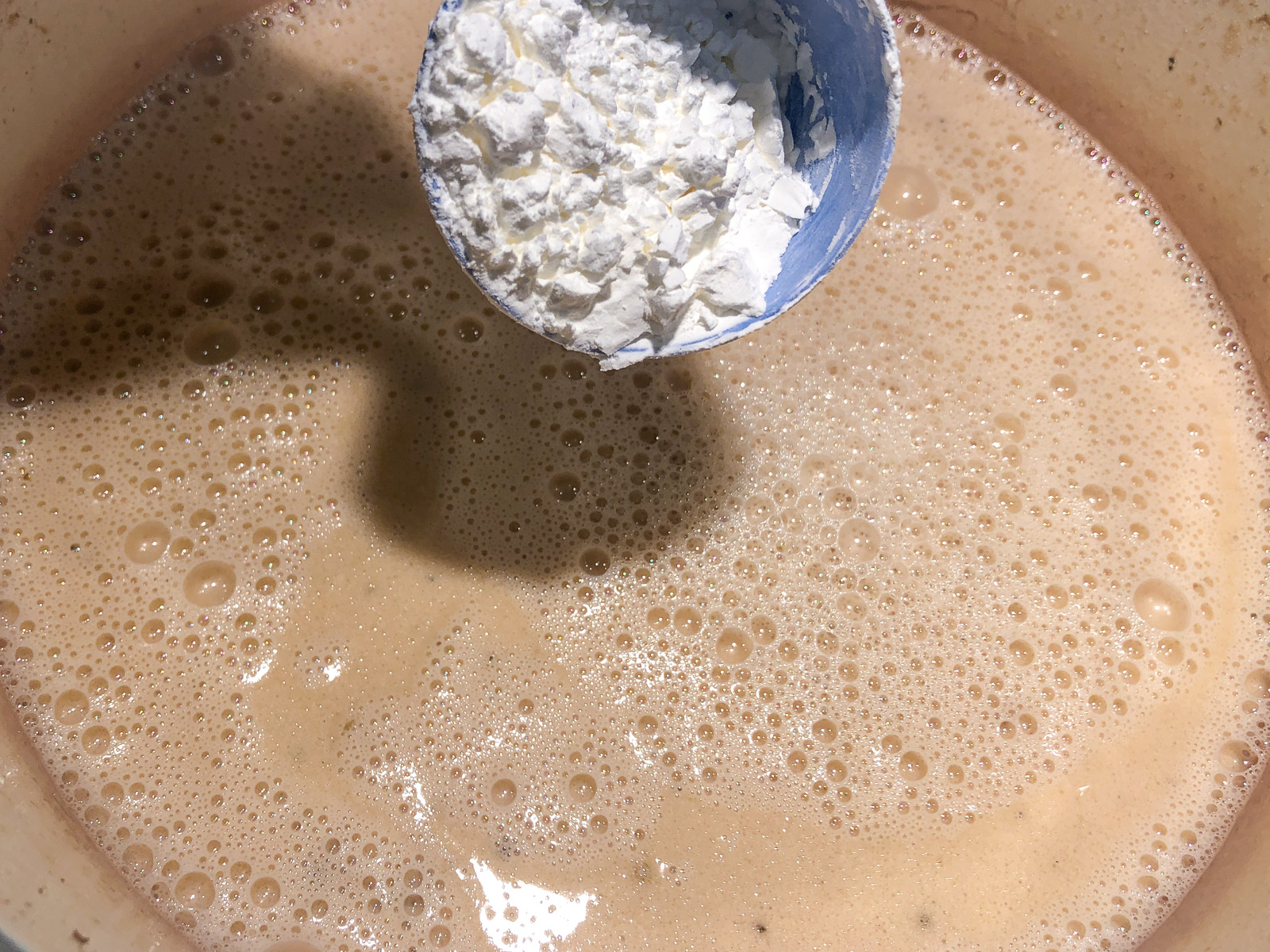 Cornstarch being whisked into the creamy cooking liquid to thicken the gravy.